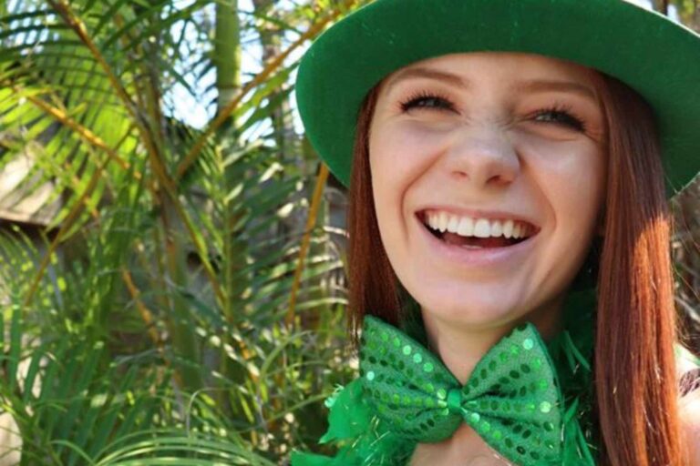 A smiling woman with a green hat and green bowtie. Luck of the Irish! Get a Gold Bucket of Beer when you stay in the month of March!