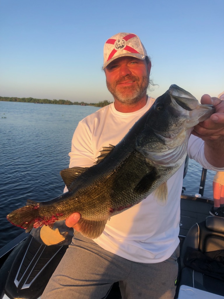 Man grinning holding a large bass out on the bass boat