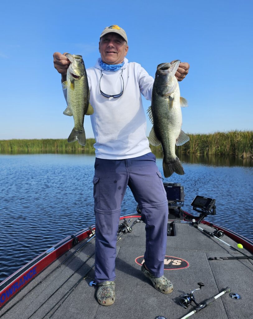 Man holding 2 bass fish that he caught on a bass boat