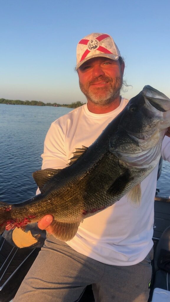 Man grinning holding a large bass out on the bass boat